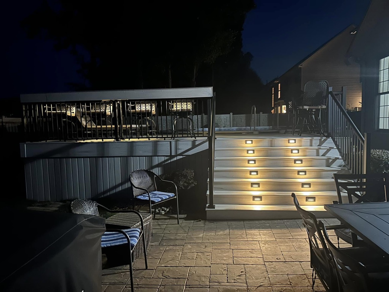 Deck stairs with lit risers over a stamped-concrete patio at night